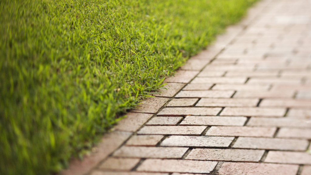 A brick walkway borders a lush green lawn, demonstrating how to prevent soil compaction by providing footpaths